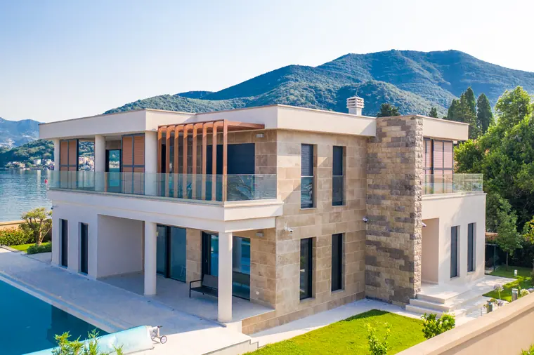 The villa's entrance elevation: travertine laid in long courses, a rough-stone corner pier, and a timber pergola over the first-floor terrace.